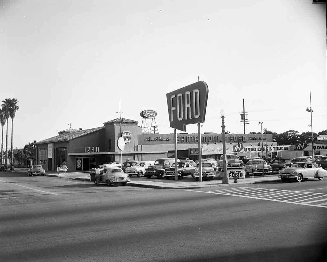 Concessionaria Ford degli anni Cinquanta con grande insegna verticale sulla strada